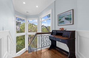 A corner room with a desk, a painting, and a view of trees through large windows. - Stunning home close to the Ocean Course (Johns Island)