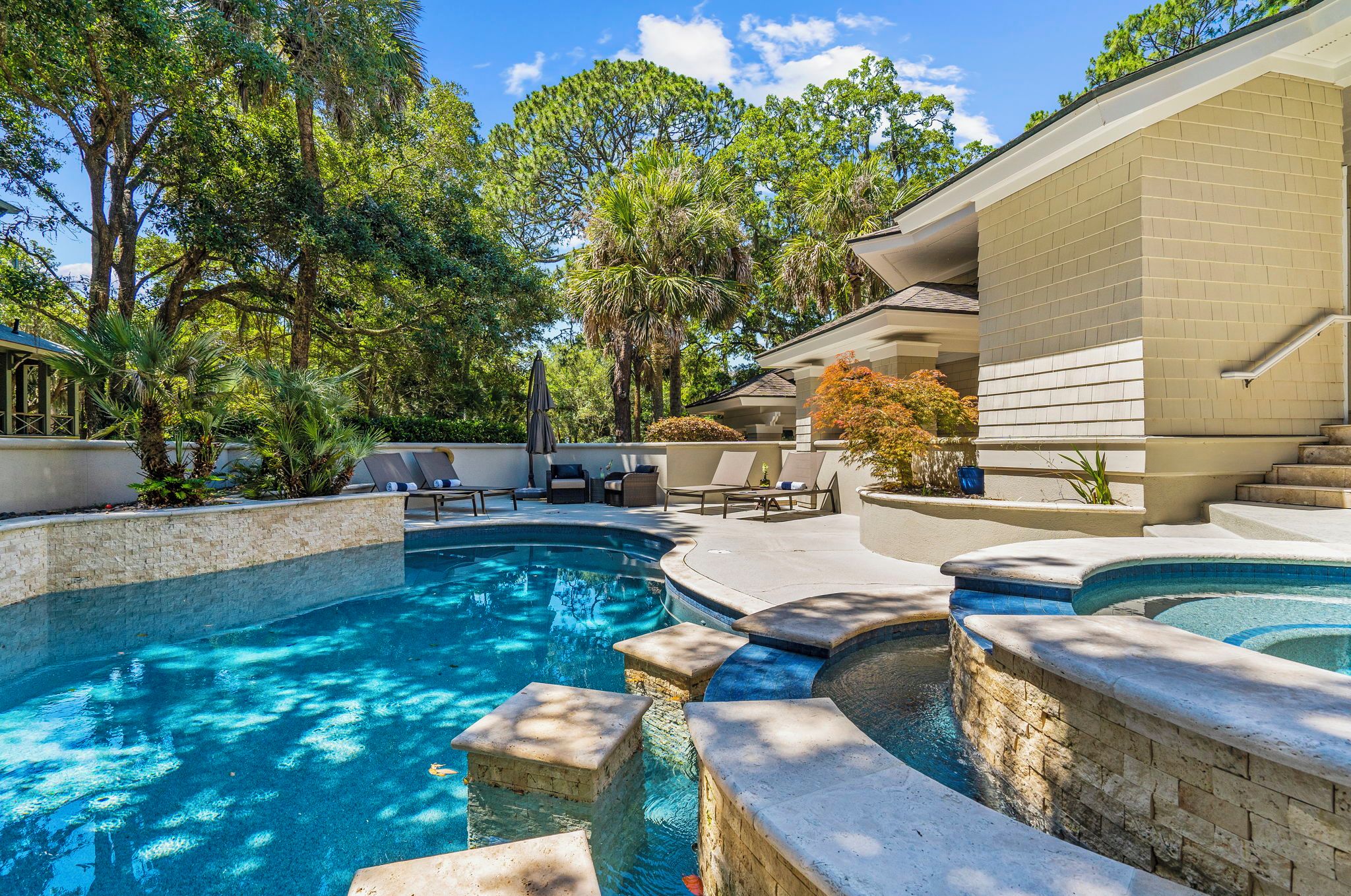 A swimming pool with a stone edge, surrounded by lounge chairs and a brick wall.