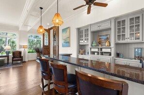 A kitchen with a bar area, wooden chairs, a ceiling fan, and cabinets with glass doors. - Stunning home close to the Ocean Course (Johns Island)