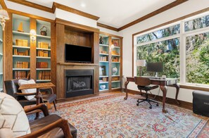 A cozy living room with a fireplace, bookshelves, a television, and a desk with a computer. - Stunning home close to the Ocean Course (Johns Island)