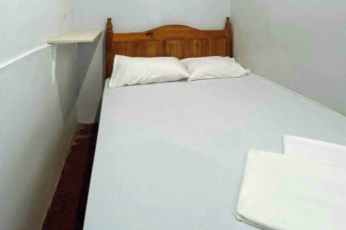 Une petite chambre avec un lit simple, une tête de lit en bois, du linge de lit blanc et une petite table de chevet.