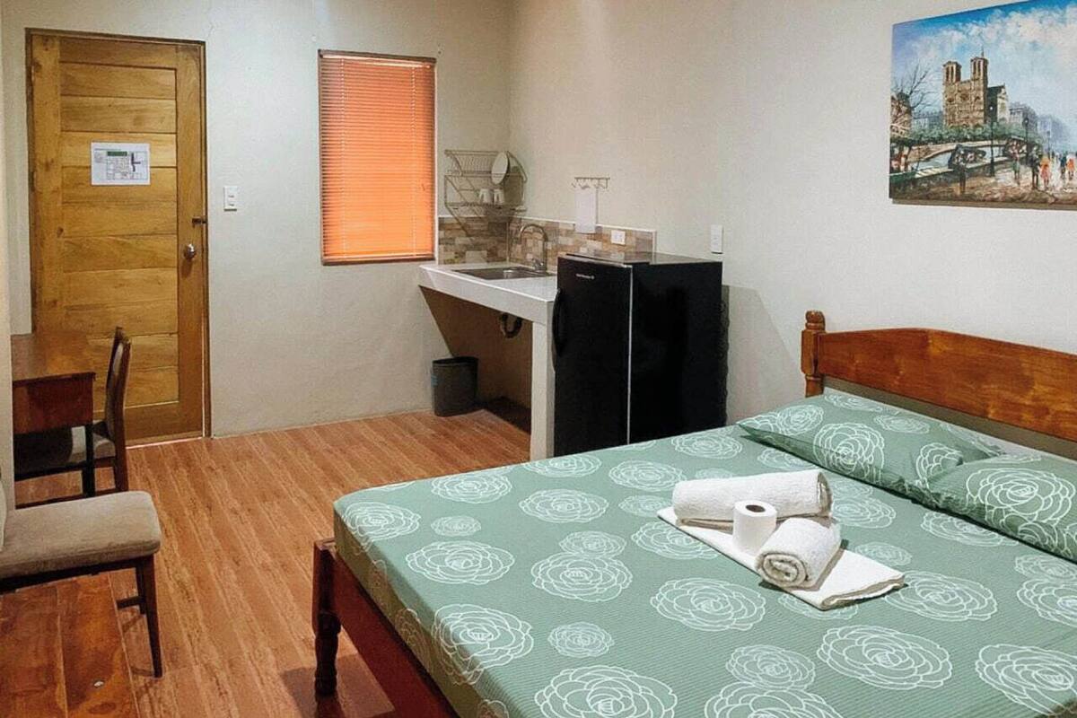 Une petite chambre comprenant un lit, un petit bureau, un réfrigérateur et une chaise.