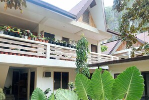 A two-story building with a balcony on the upper floor, surrounded by large green plants and potted plants. - Urbanview @ Bnky Bed And Breakfast Palawan (El Nido)