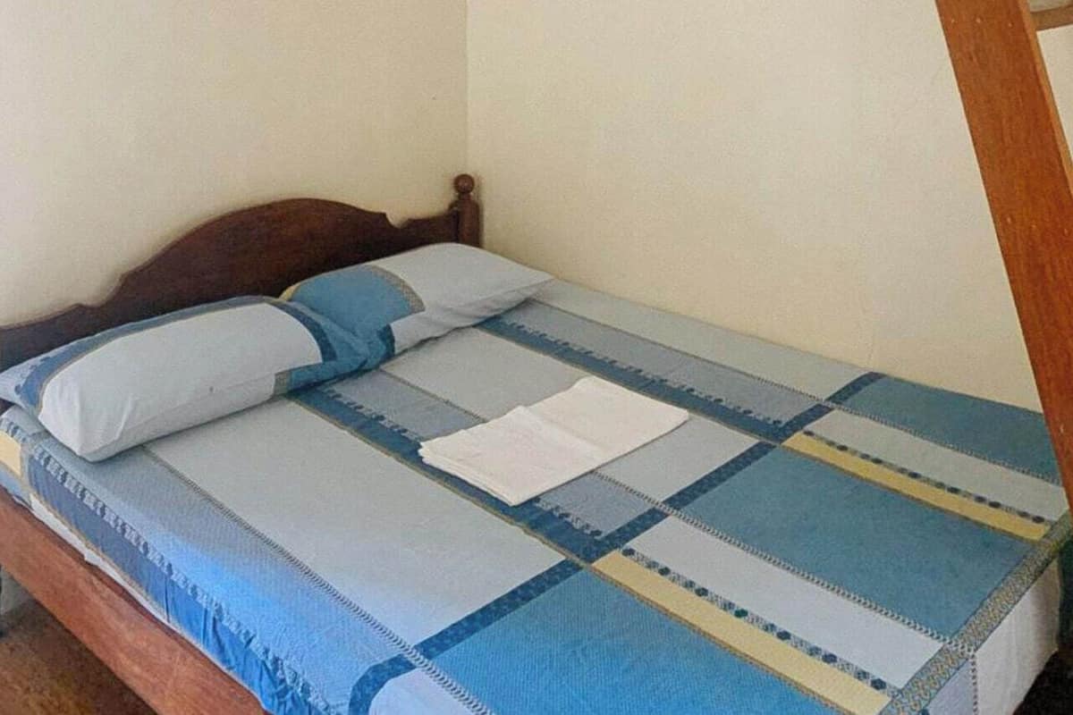 Un lit simple avec une tête de lit en bois, une couvre-lit à rayures bleues et blanches, et un oreiller blanc.
