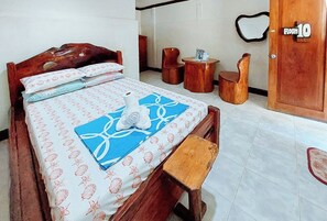 Una cama bien hecha con una colcha estampada con motivos florales, un banco de madera, una mesita de madera y un espejo montado en la pared.