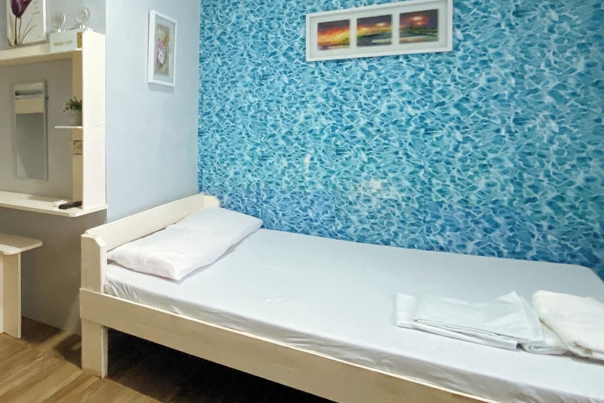 Une chambre avec un lit simple, un mur décoré de mosaïques bleues, une petite table de chevet et un tableau encadré au-dessus du lit.