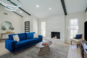 A modern living room with a blue sofa, a fireplace, and a round coffee table. - Perfect Getaway Home w Pool, Jacuzzi, Cinema Room (Richardson)