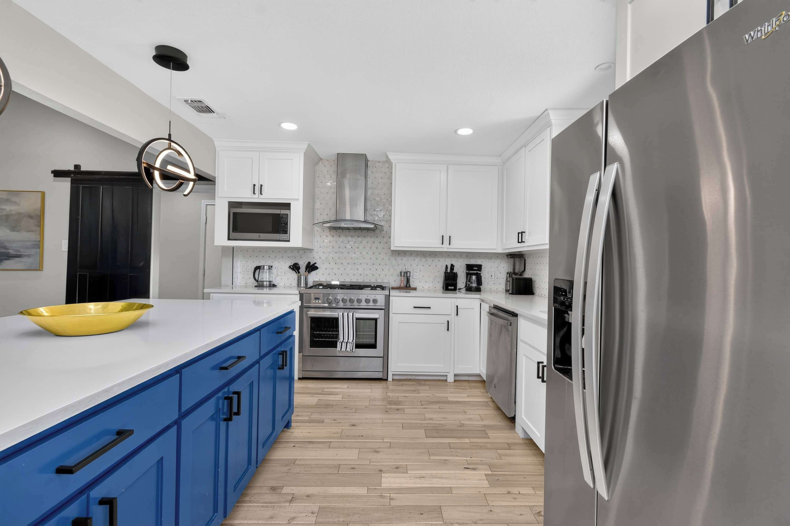 A modern kitchen with white cabinets, a stainless steel refrigerator, a yellow bowl on the counter, and a wooden floor.