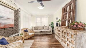 A living room with a sofa, wicker chairs, a wooden cabinet with a mirror, and a ceiling fan. - Seven Smiles, Gerroa, South Coast (Gerroa)