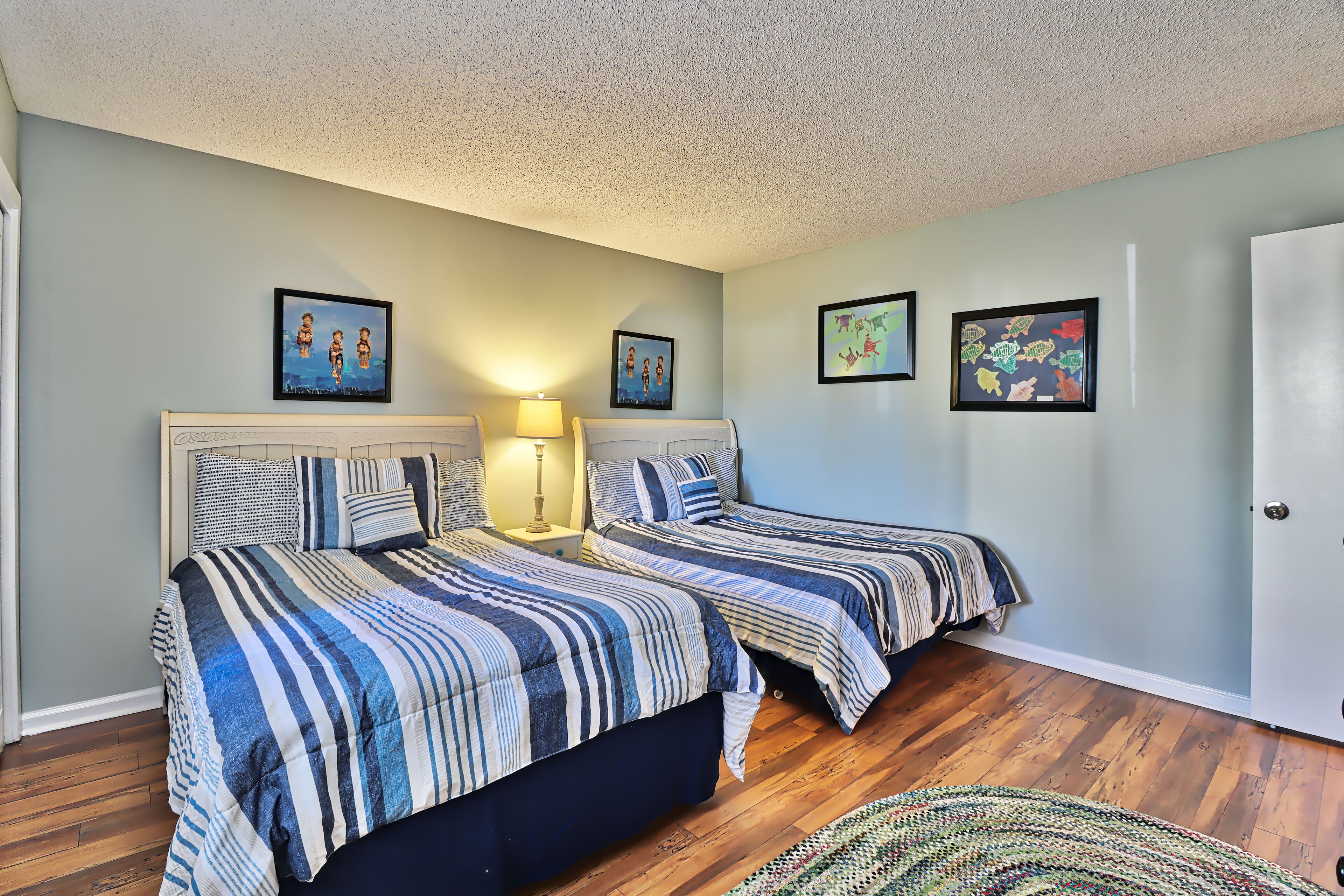 A bedroom with two beds, a nightstand with a lamp, and framed artwork on the walls.