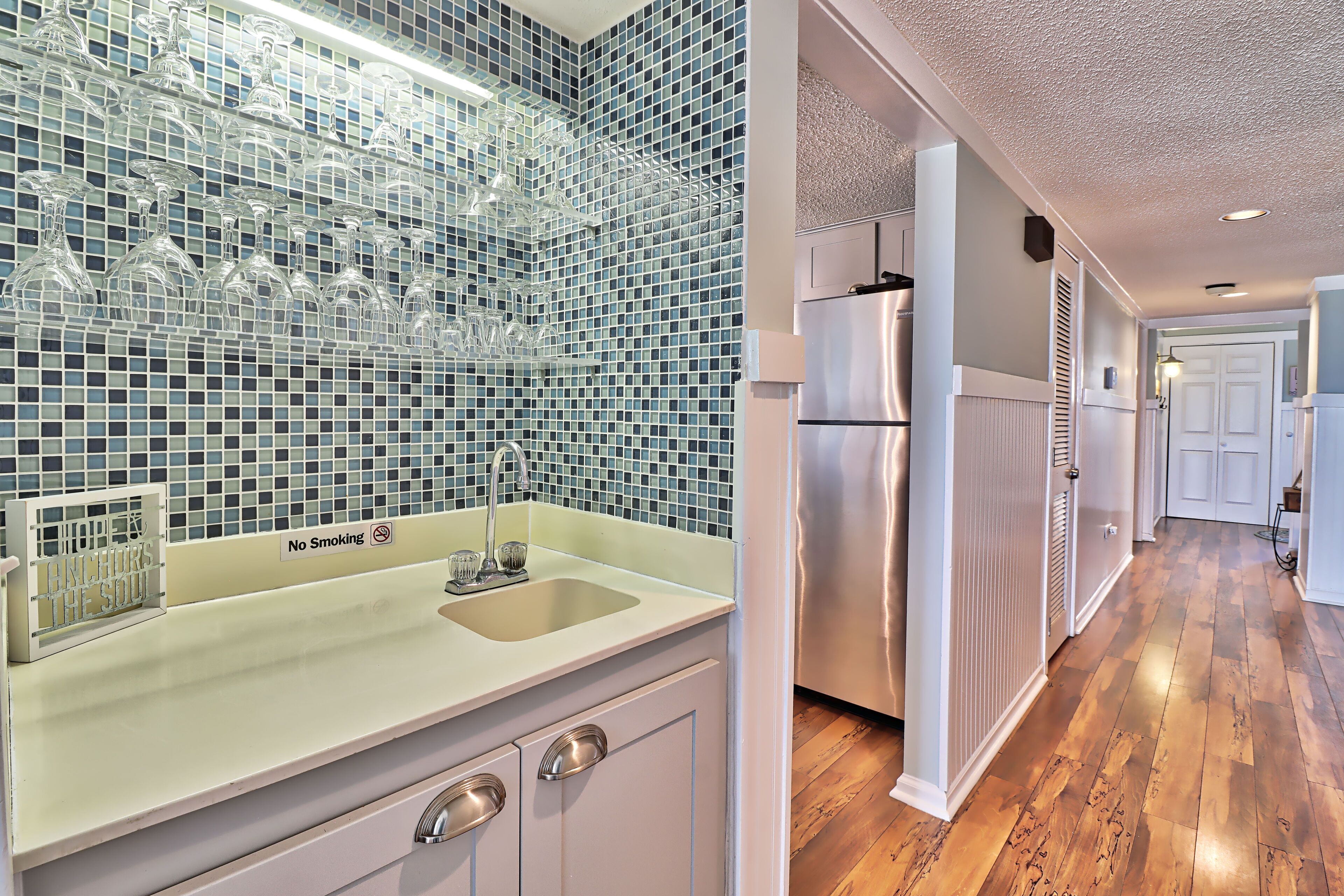 A kitchen with a tiled backsplash, a stainless steel refrigerator, and a sink with a 'No Smoking' sign.