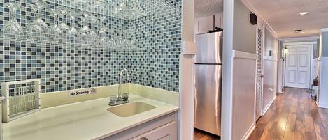 A kitchen with a tiled backsplash, a stainless steel refrigerator, and a sink with a 'No Smoking' sign.