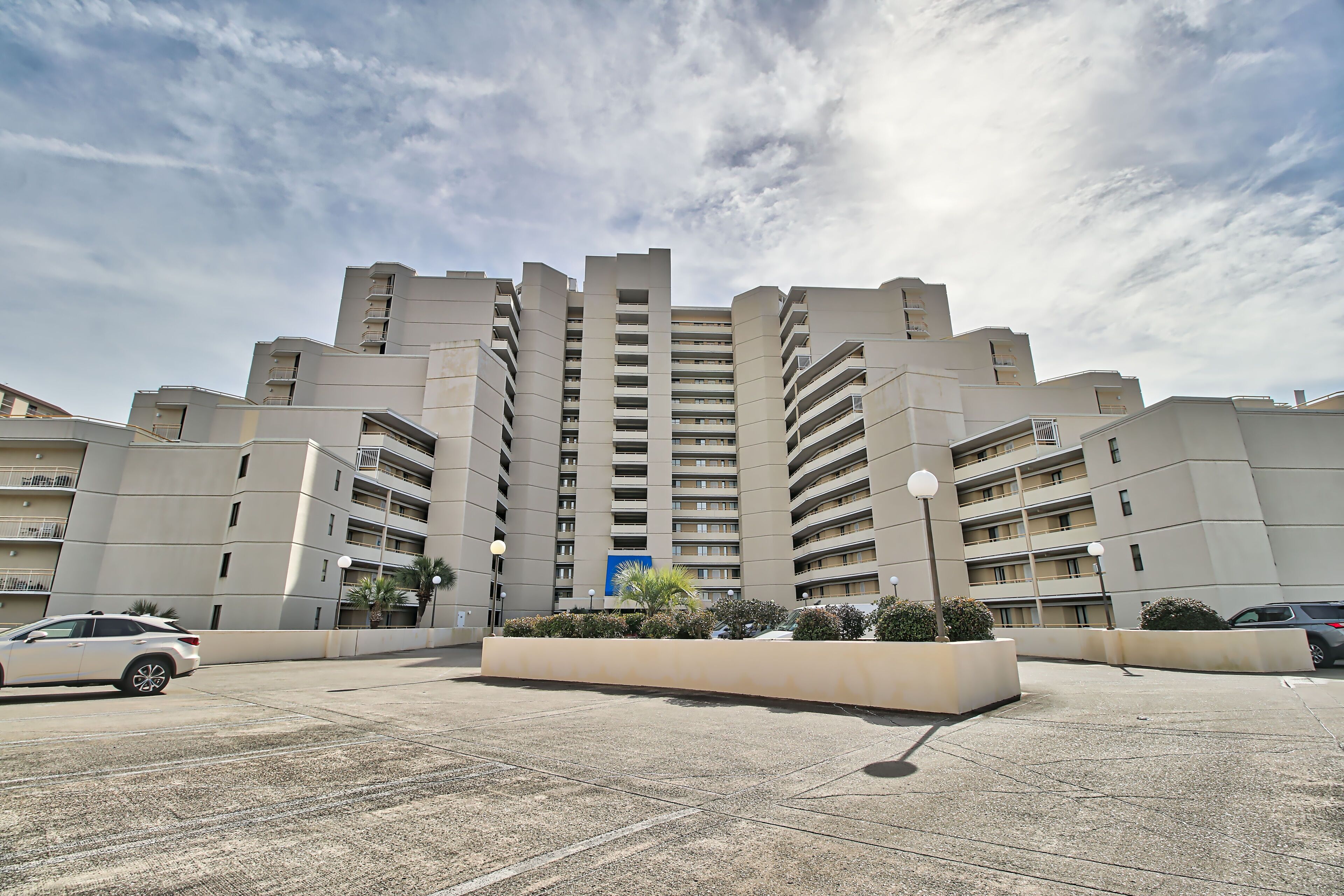 A modern multi-story residential building with a central courtyard, balconies, and a parking area.