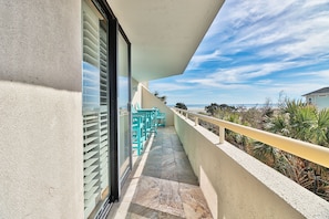 A balcony with a view of the ocean, a railing, and outdoor furniture.