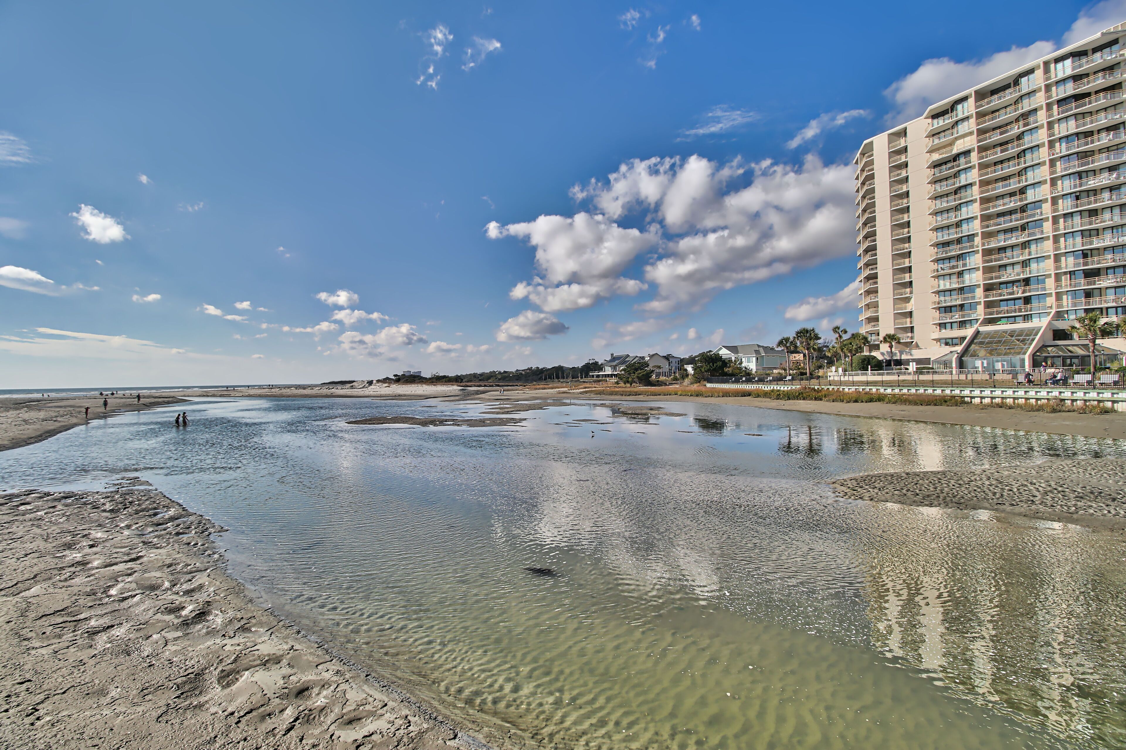Et hotel ved stranden med en stor swimmingpool, klare himmel og en sandstrand.