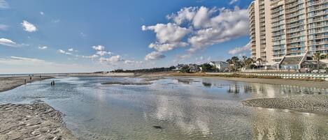 Et hotel ved stranden med en stor swimmingpool, klare himmel og en sandstrand.