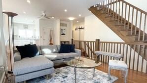 A modern living room with a grey sectional sofa, a glass coffee table, and a wooden staircase. - Luxury Sea Bright Home, Ocean Views, 6 Sun Decks! (Sea Bright)
