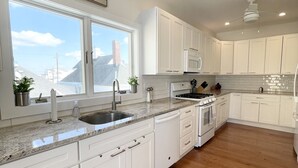 A modern kitchen with white cabinets, a granite countertop, and a view of the city through large windows. - Luxury Sea Bright Home, Ocean Views, 6 Sun Decks! (Sea Bright)