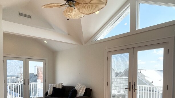 A spacious living room with a large ceiling fan, a dark-colored sofa, and a view of a balcony through large sliding glass doors. - Luxury Sea Bright Home, Ocean Views, 6 Sun Decks! (Sea Bright)