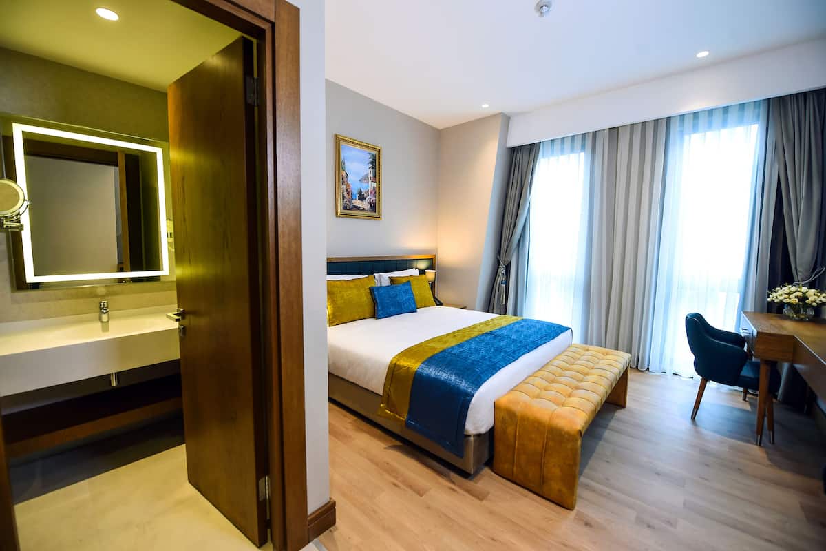 A hotel room with a bed, bedside table, chair, and a desk with a chair.