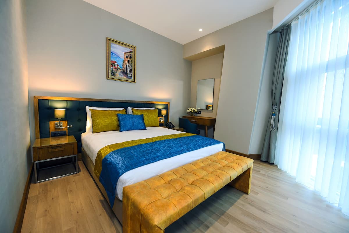 A hotel room with a large bed, bedside tables, a desk, and a window with curtains.