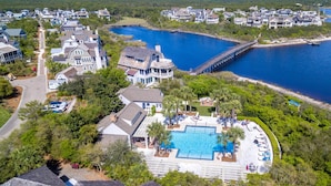 An aerial view of a coastal resort with multiple buildings, a large swimming pool, and a pier extending into the water. - Family Retreat with Pool and Golf Cart (Watersound)
