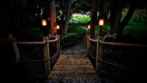 A wooden bridge with rope railings leading to a path surrounded by trees. - Emlyn's Coppice - Woodland Glamping (Holywell)