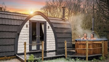 Una cabaña rústica con un jacuzzi de madera, una chimenea y una terraza de madera.