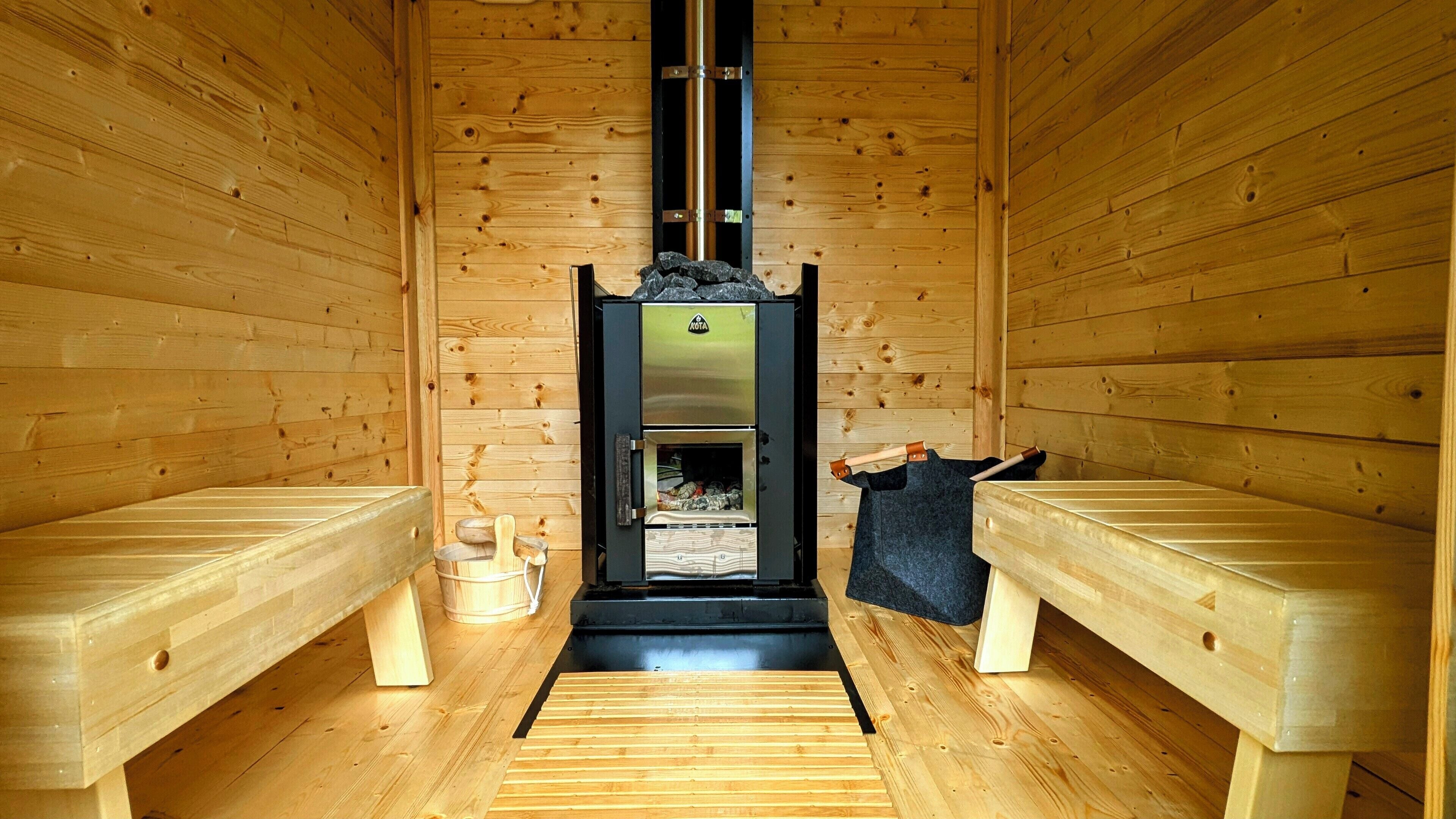 Een sauna met houten banken, een sauna-unit en een houten vloer.