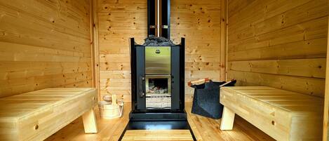 A sauna room with wooden benches, a sauna unit, and a wooden floor.