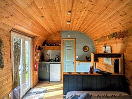 Interior acogedor de una cabaña de madera con kitchenette, cama y puerta que da a un balcón.