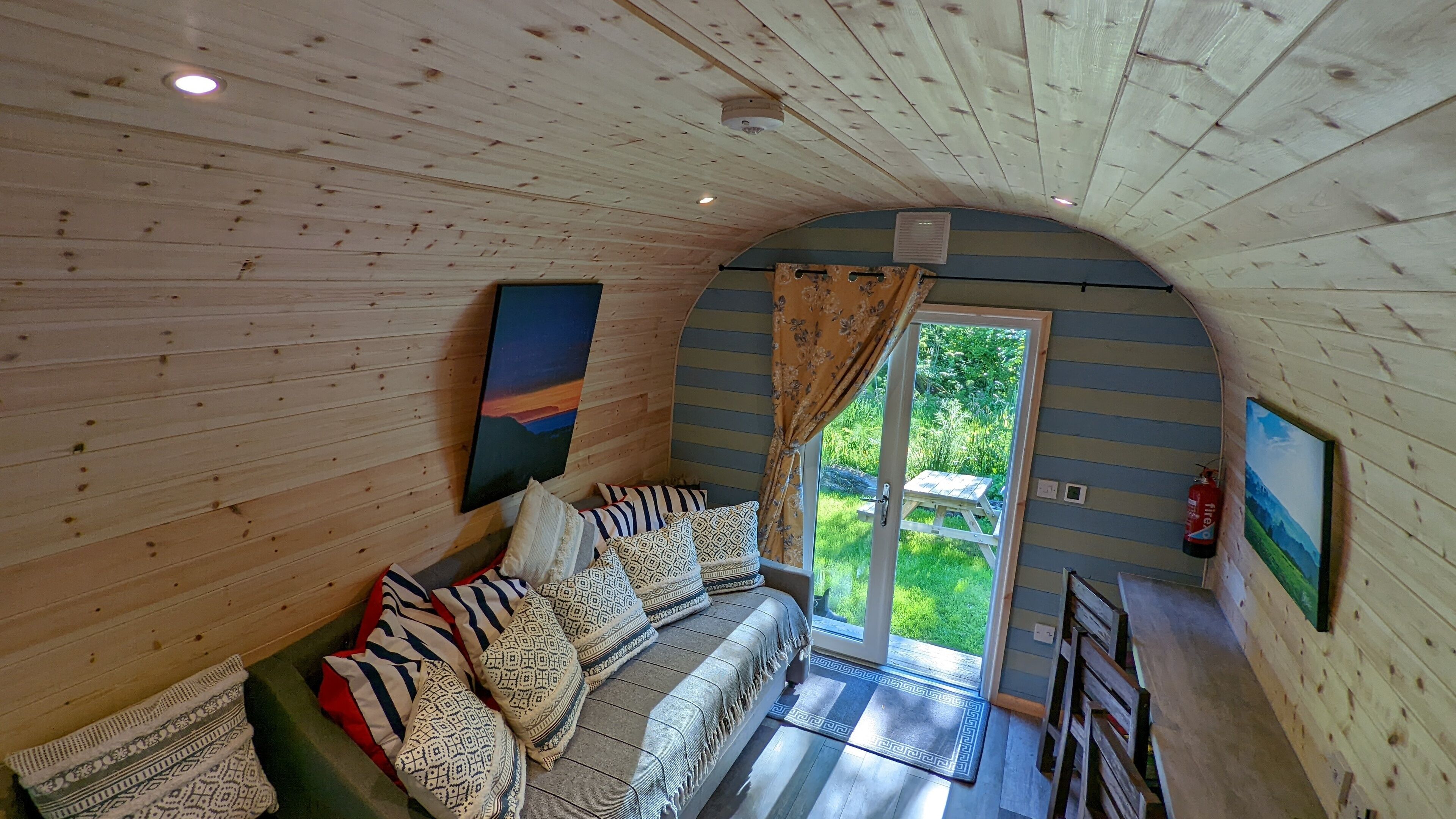 L’intérieur d’un chalet en bois, avec un canapé, des coussins à motifs et un tableau accroché au mur.