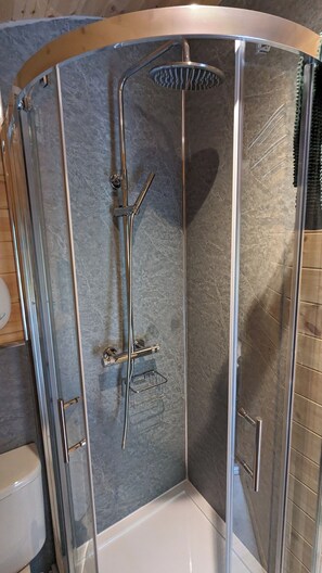 Cabina de ducha con paredes de vidrio, ducha de mano y grifo empotrado.