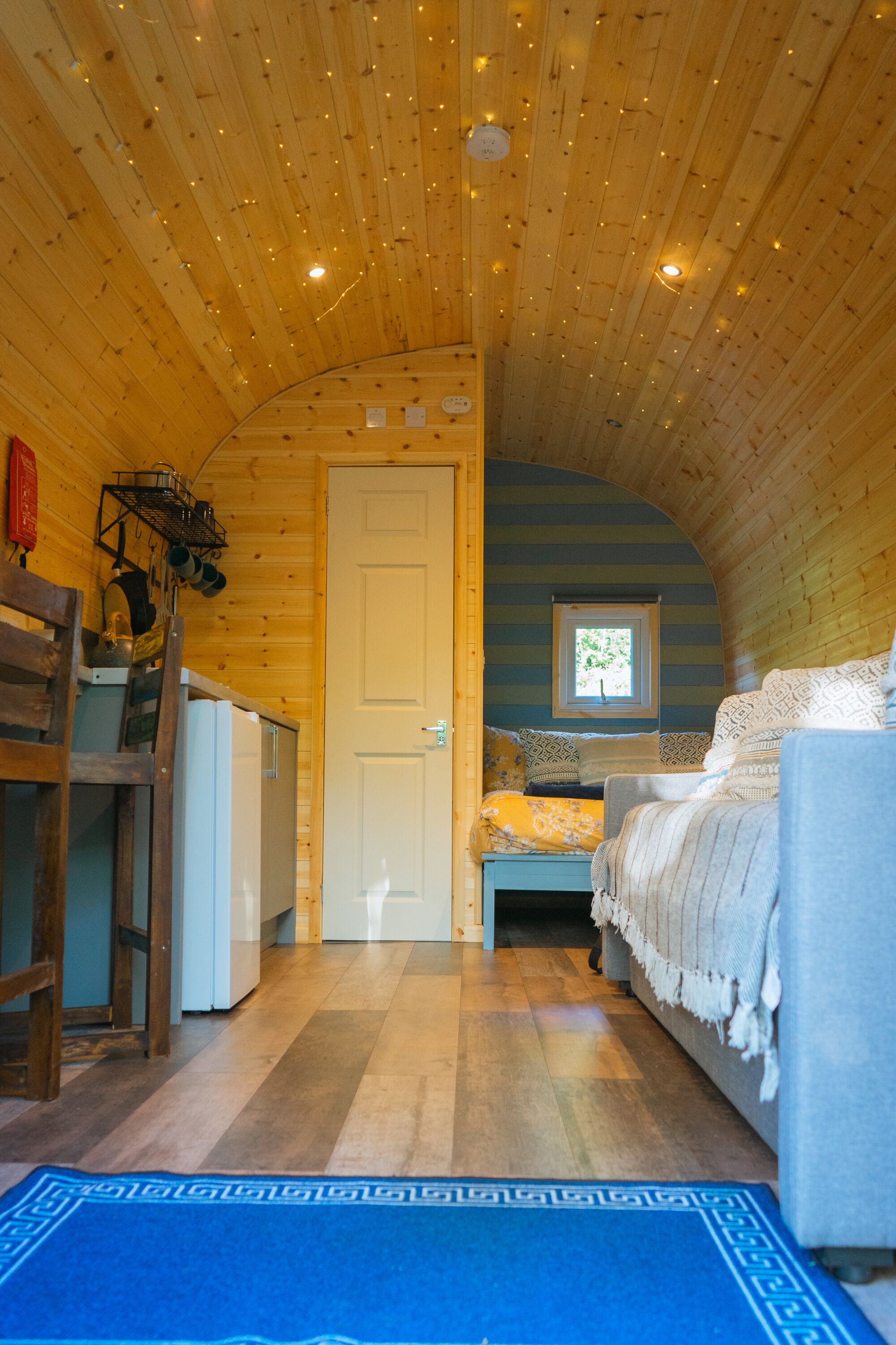 A cozy cabin with a wooden interior, a bed, a small window, and a kitchenette.