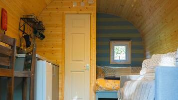 Une cabane confortable avec un intérieur en bois, un lit, une petite fenêtre et un coin cuisine.