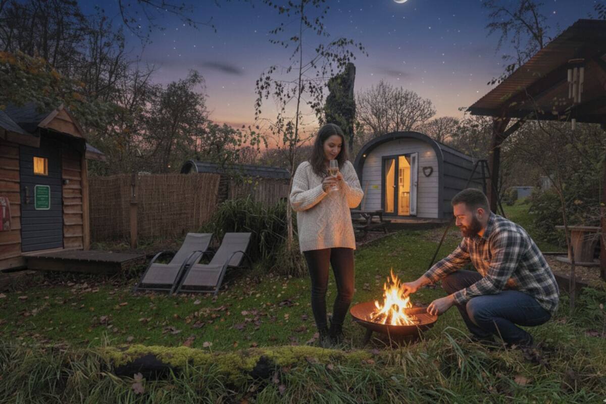 Un entorno rústico al aire libre con una fogata, sillones de descanso y una pequeña cabaña.