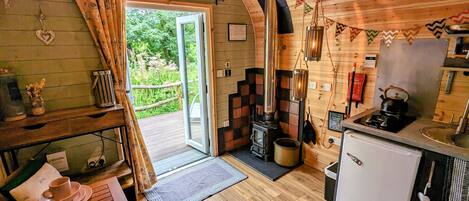 A cozy cabin with a wooden interior, a fireplace, a small kitchen, and a view of the surrounding greenery.