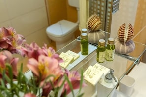 Une salle de bain avec une étagère en verre où sont exposés des articles de toilette, des toilettes et un miroir qui reflète un coquillage.
