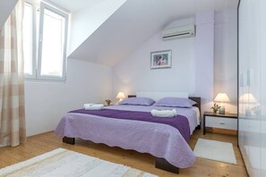 Un dormitorio con cama, dos mesitas de noche, una ventana, un equipo de aire acondicionado y un cuadro colgado en la pared.