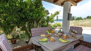 An outdoor dining area with a table set for breakfast, surrounded by chairs and a large tree. - Beachfront Holiday House Zita (Brgulje)