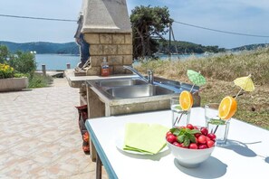 Une cuisine extérieure équipée d’un évier et d’une table où sont disposés un saladier de cerises, des verres d’eau et une serviette.