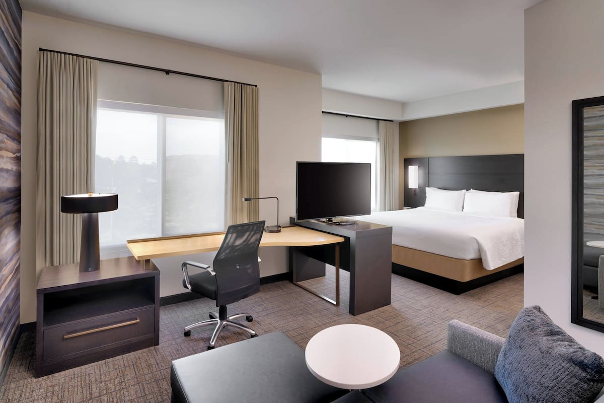 A hotel room with a bed, desk, chair, and a small table.