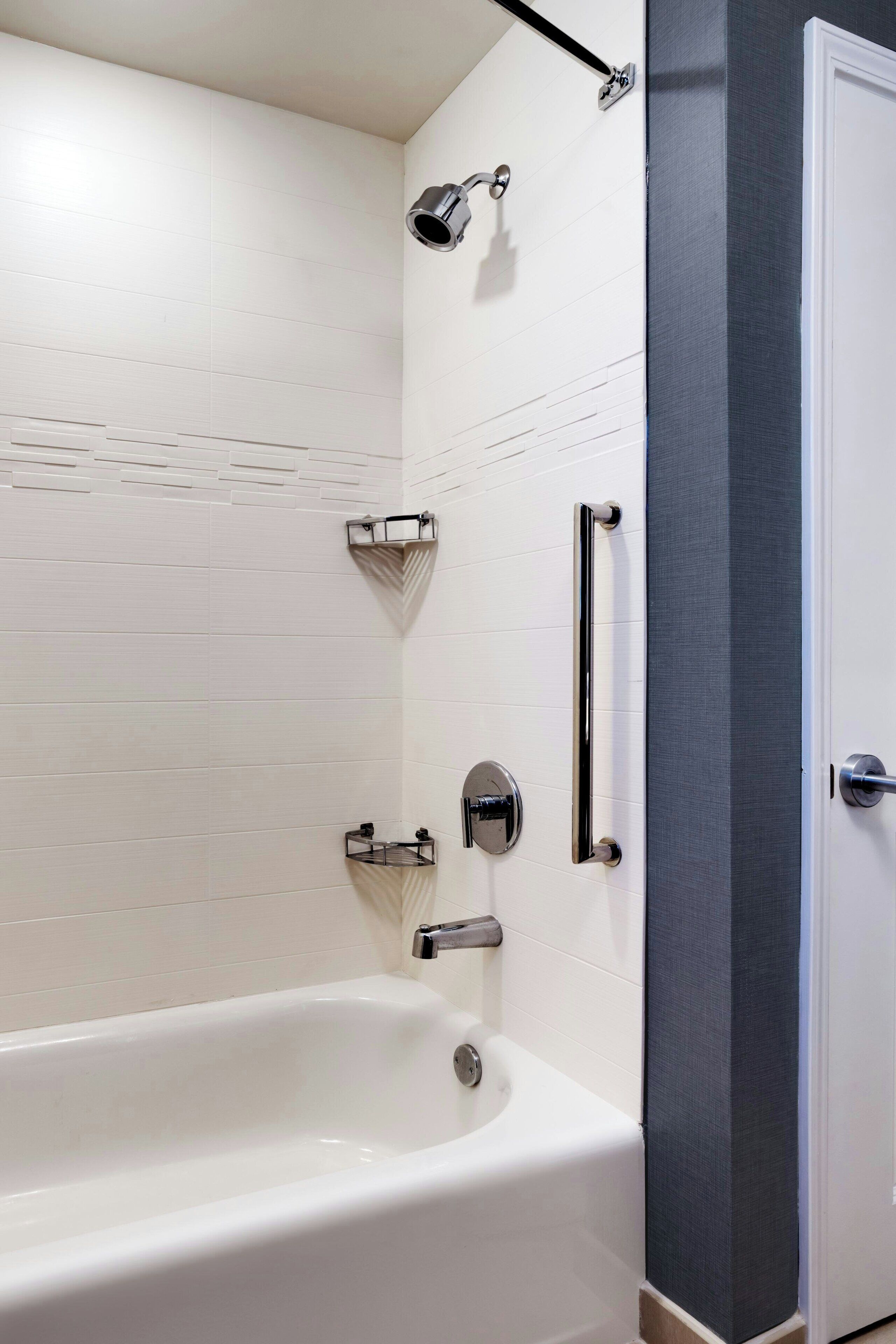 A bathroom with a white bathtub, a shower with a handheld showerhead, and a door with a textured panel.