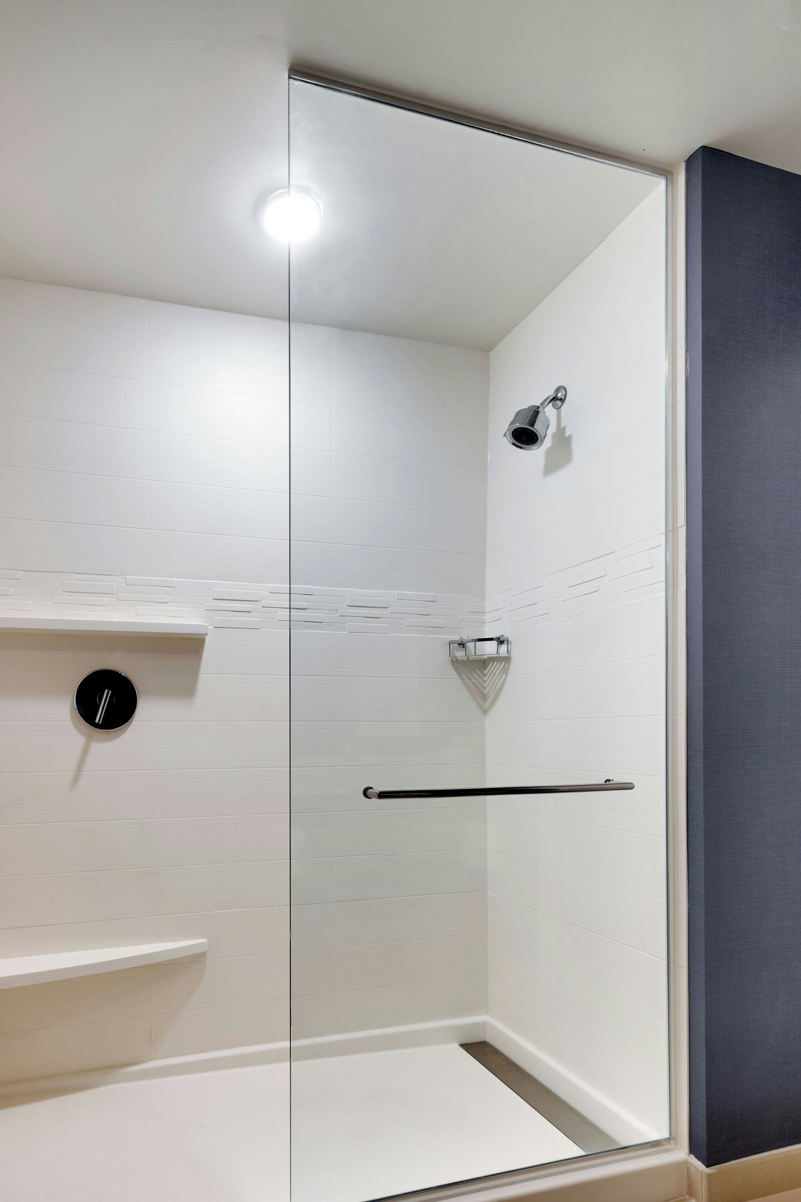 Une douche fermée par des parois en verre, dotée d’un pommeau de douche à main, d’un porte-serviettes et d’une petite étagère.
