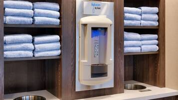 Ein Badezimmer mit Handtuchspender, Regalen mit ordentlich gefalteten Handtüchern und einem Mülleimer.