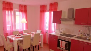 Une cuisine avec des meubles de couleur rouge, un plan de travail blanc et un coin repas avec une table dressée pour quatre personnes.