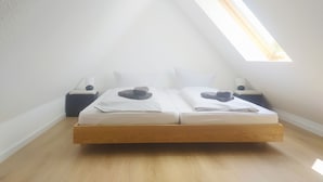 A bedroom with a sloped ceiling, a skylight, a bed with white linens, and two bedside tables.