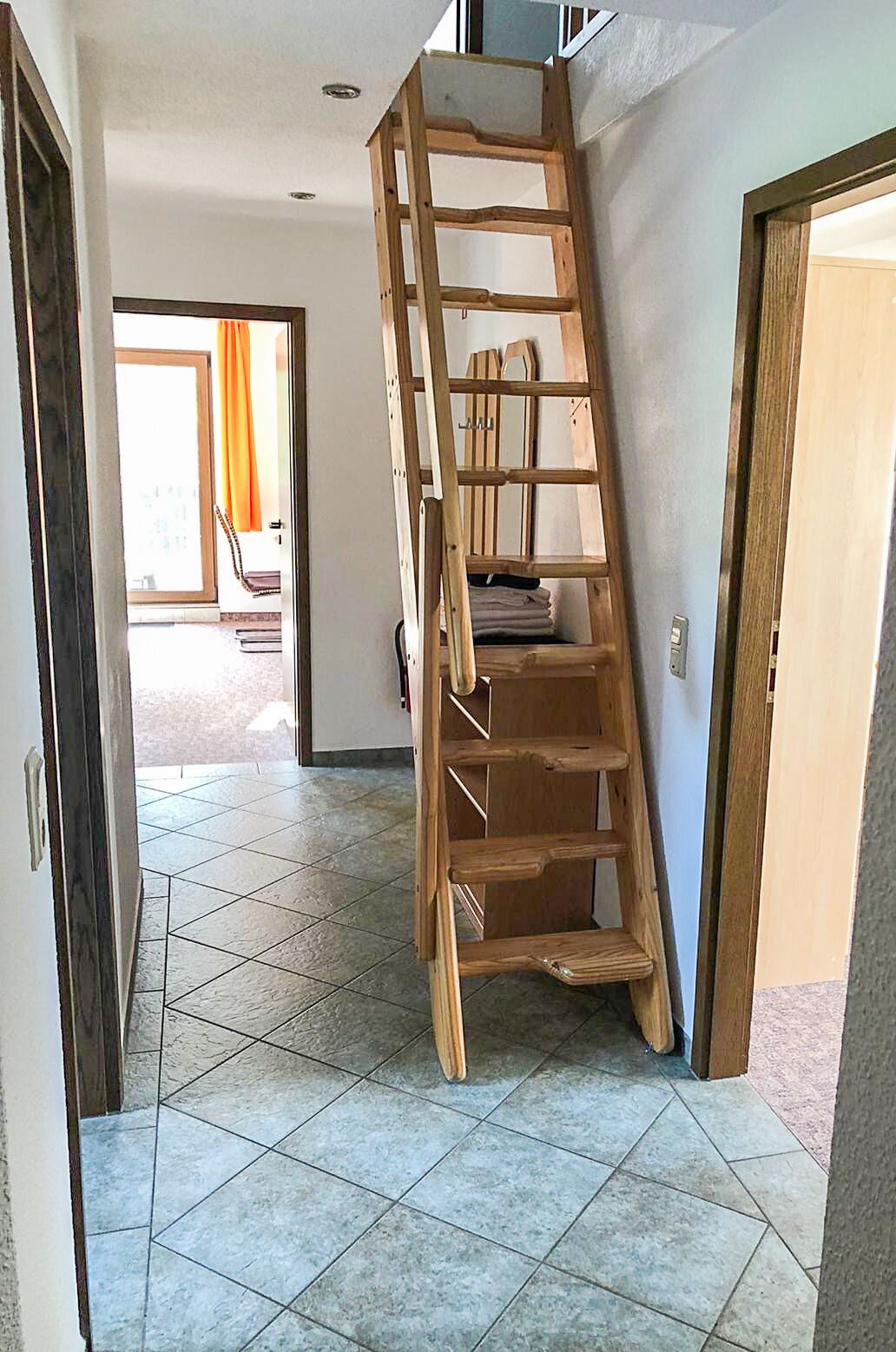 A wooden ladder in a hallway with tiled flooring and a door leading to another room.