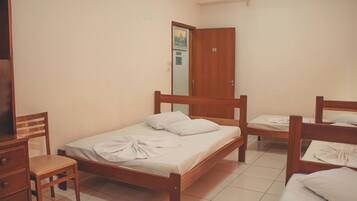 Quarto com duas camas de madeira, cômoda de madeira e uma porta com número.