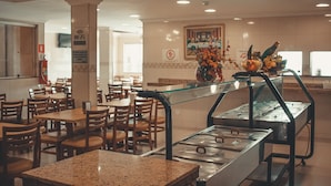 A cafeteria with multiple tables and chairs, a buffet area with a glass display case, and a WiFi sign on a pillar. - Hotel Piracicaba (Aparecida)